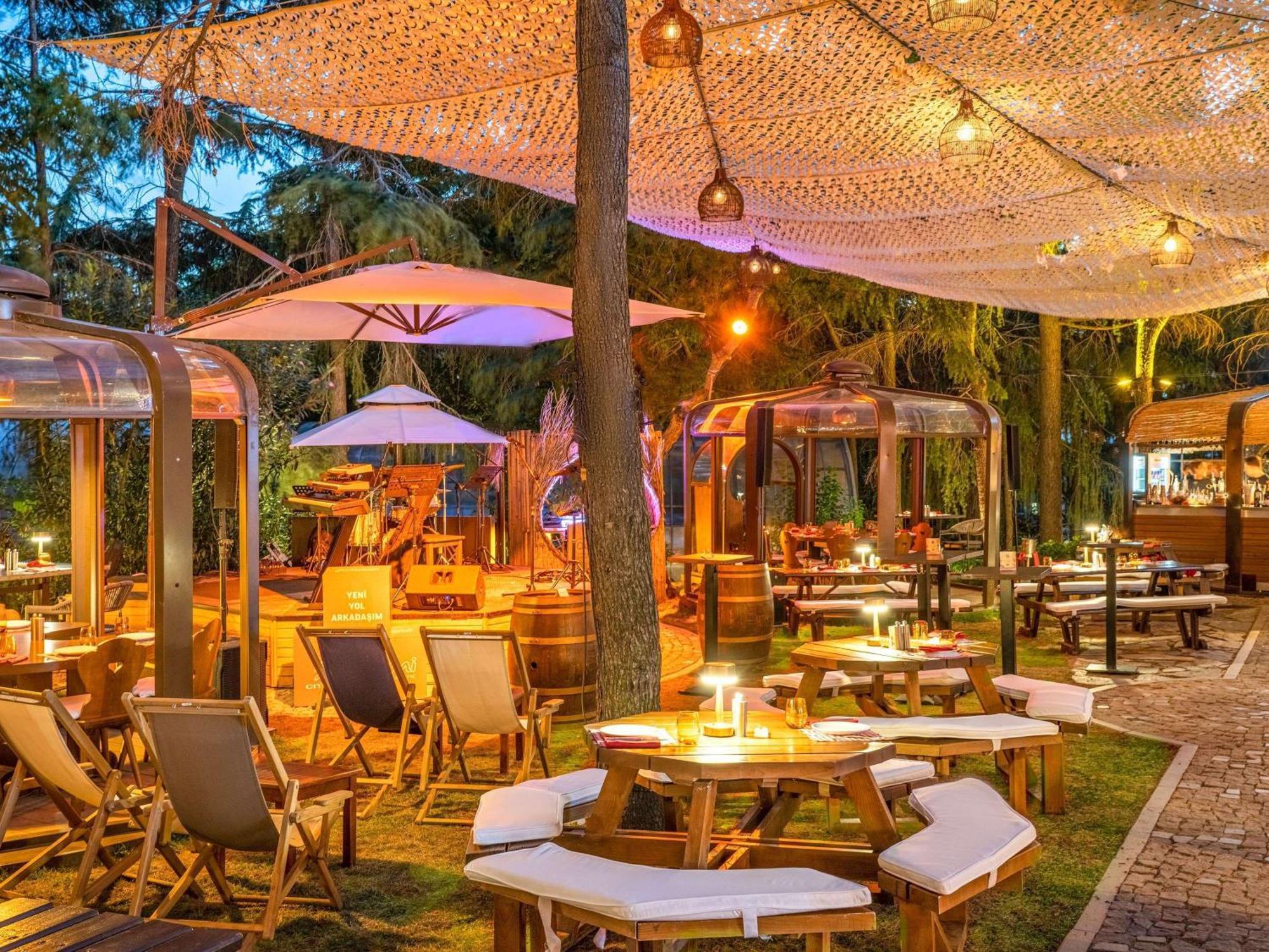 Swissotel The Bosphorus Istanbul Eksteriør billede The photo depicts a beautifully arranged outdoor dining space. There are wooden tables and chairs arranged across a grassy area, some featuring cozy seating. Large umbrellas provide shade, and there are unique, transparent structures, possibly for di