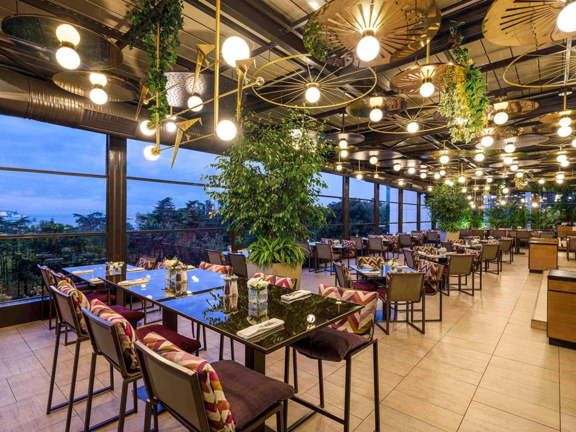 Swissotel The Bosphorus Istanbul Eksteriør billede The photo shows a stylish restaurant interior with a modern design. It features several long tables with chairs arranged neatly. The atmosphere is enhanced by large windows that provide a view of the outside. The ceiling is adorned with unique light 