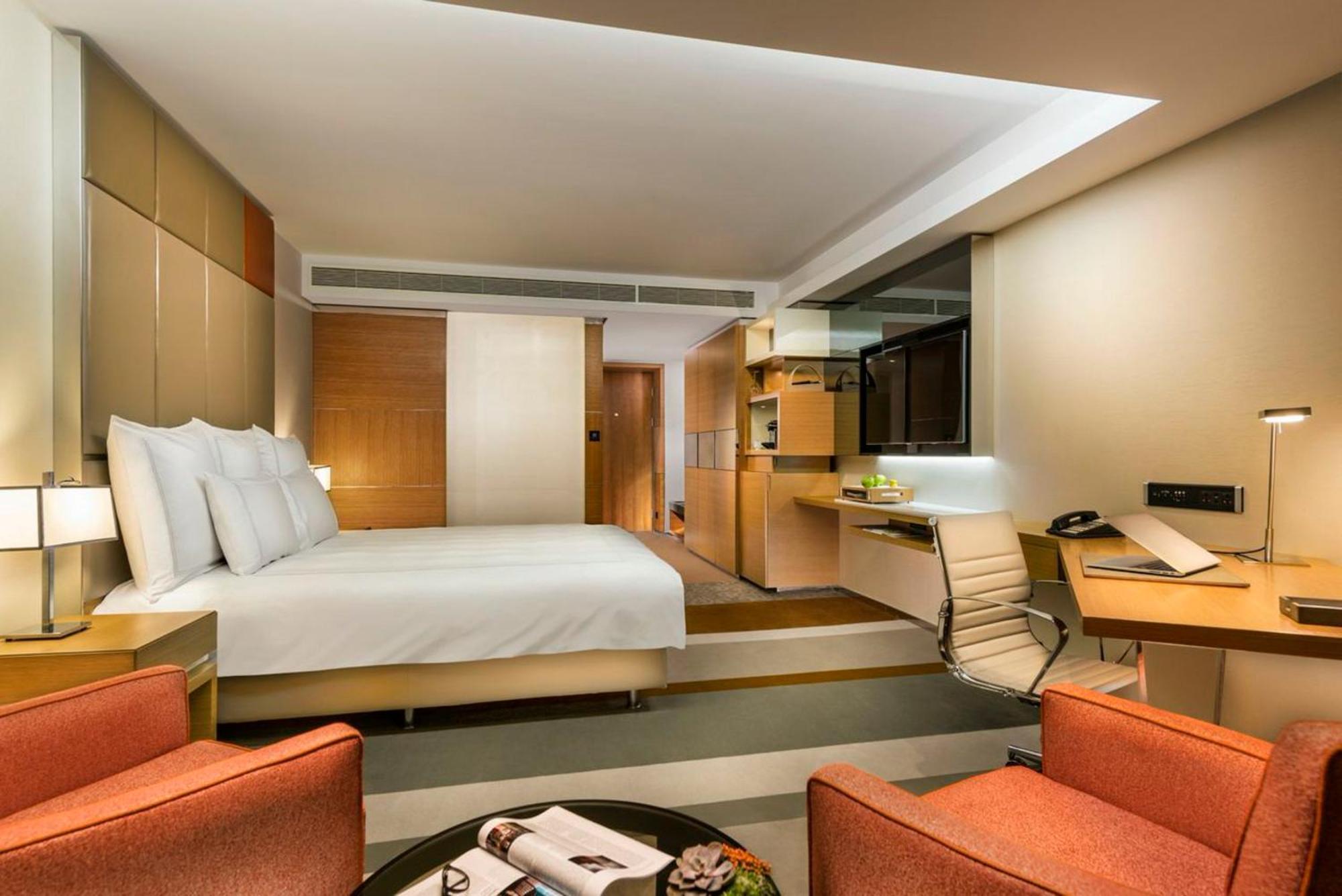 Swissotel The Bosphorus Istanbul Eksteriør billede The photo shows a modern hotel room featuring a comfortable king-sized bed with white bedding. There are two bright orange armchairs positioned beside a round coffee table that holds a magazine. The room has a contemporary design, with light wood acc