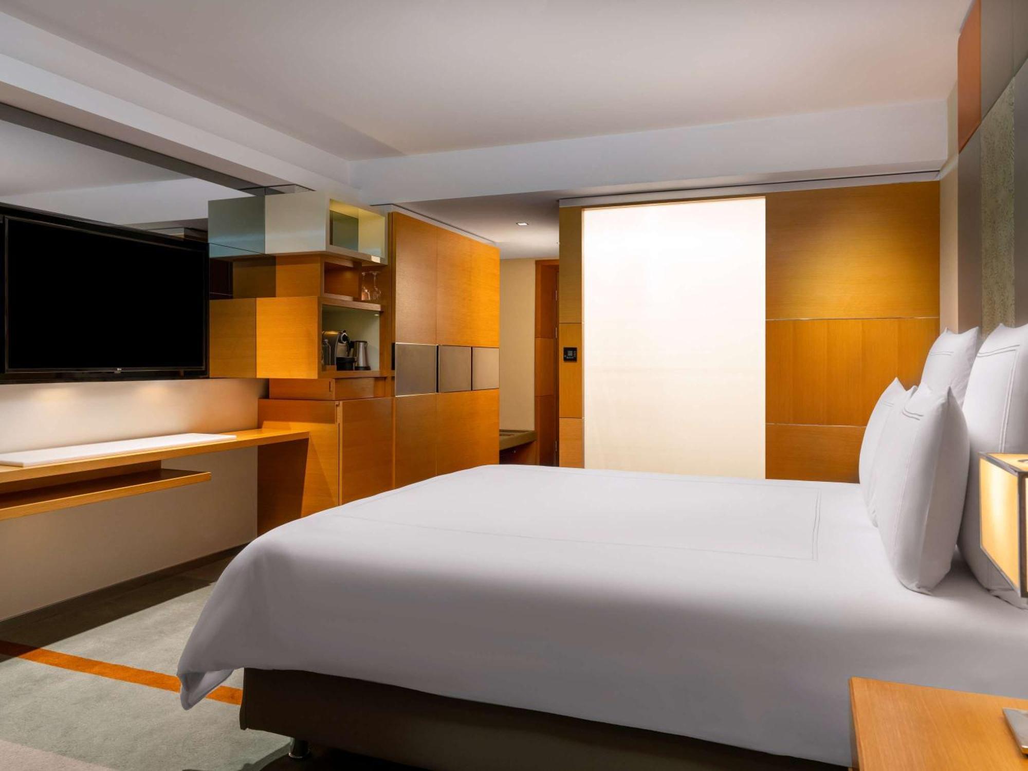 Swissotel The Bosphorus Istanbul Eksteriør billede The photo shows a modern hotel room. It features a large bed with white linens and pillows at the forefront. The walls and furniture have a warm, wooden finish, giving the space a cozy and contemporary feel. To one side, there is a flat-screen televi