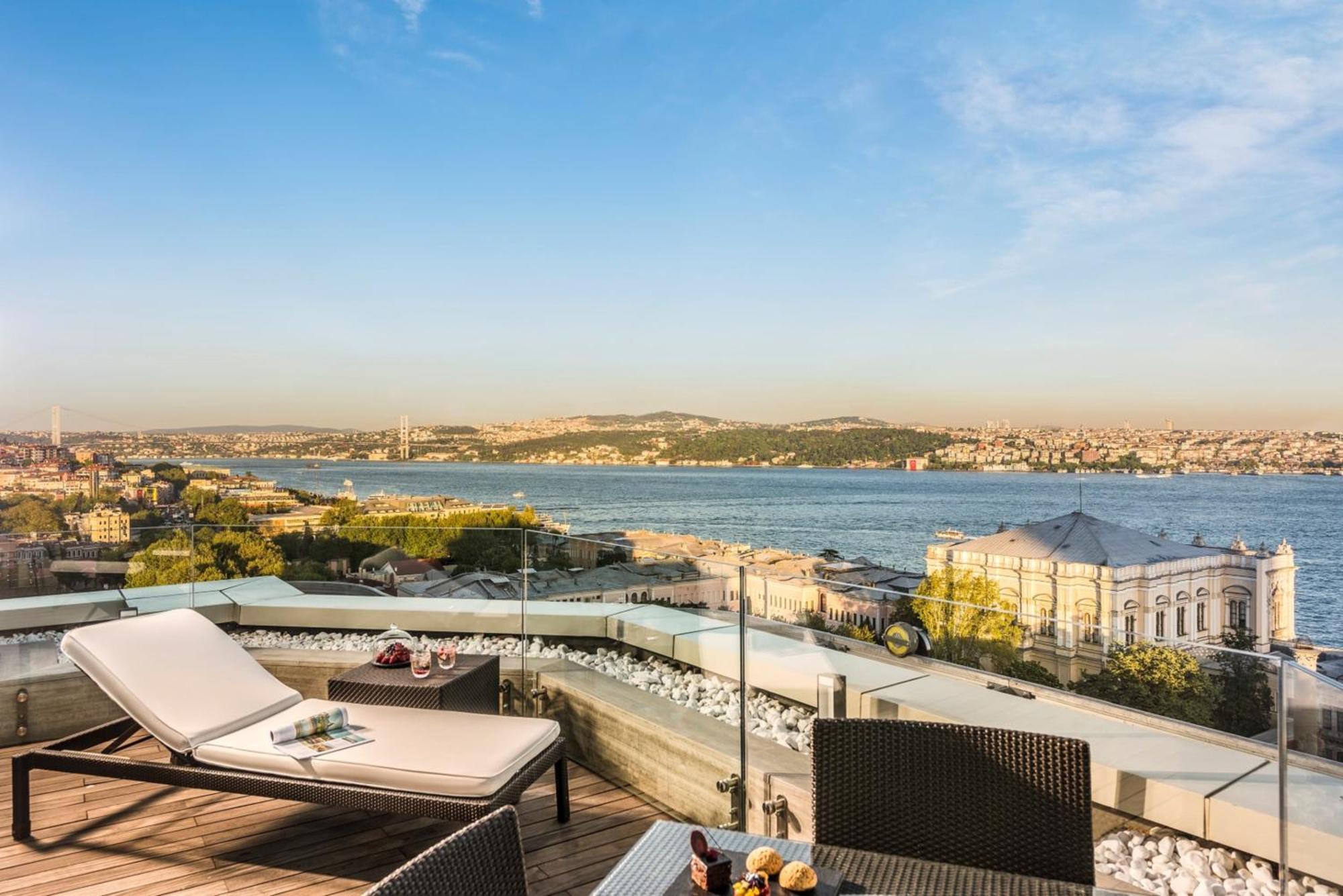 Swissotel The Bosphorus Istanbul Eksteriør billede The photo shows a scenic view from a balcony or terrace overlooking a river or body of water. There are two lounge chairs positioned on the deck, surrounded by a modern and stylish setup featuring a small table. The landscape includes distant hills o